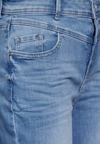 Vaaleansiniset farkut, joissa on sileä pinta, viisi taskua ja kontrastiväriset saumat. Sisältää pienen kolikkotaskun ja veto- vetoketjun.