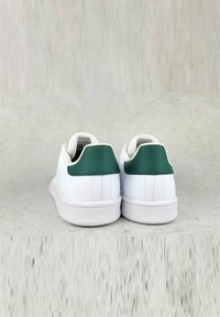 Sneakers bianchi con finitura in pelle liscia e con un tab sul tallone verde. Forma arrotondata e suola in gomma testurizzata, design minimalista.