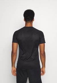 Camiseta atlética negra de manga corta, textura suave, cuello redondeado y costuras de hombro raglán. Presenta un diseño ligeramente ajustado.