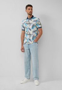 Koszula polo z krótkim rękawem w kolorze białym, z niebieskim i beżowym wzorem liści. Posiada granatowy kołnierzyk i mankiety. Połączona z jasnoniebieskimi dżinsami i białymi sneakerami.