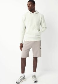 Jasnoszary polarowy hoodie z kieszenią kangurką, w połączeniu z beżowymi szortami sportowymi i szarymi trampkami z białymi akcentami. Gładka faktura.