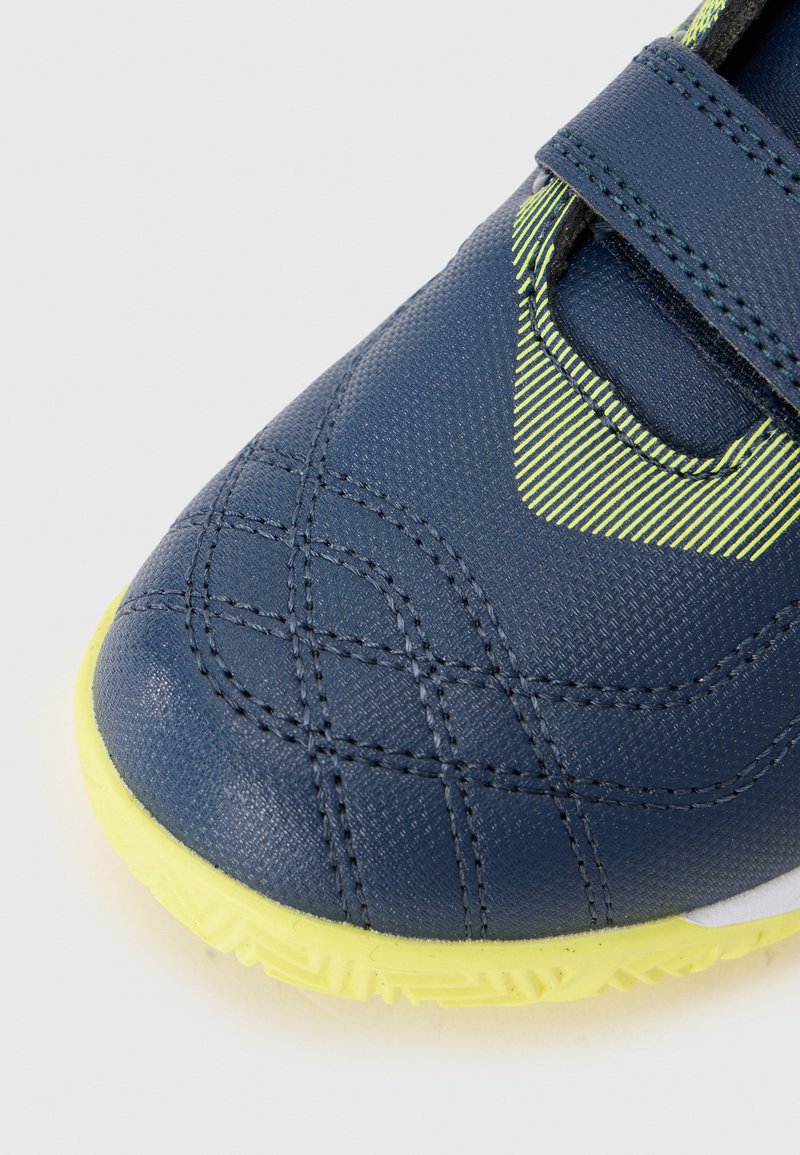 Zapatilla deportiva azul con un upper texturizado, acentos amarillos y correa de Velcro. Presenta detalles y una suela de goma para tracción.