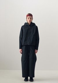 Black outdoor jacket with a hood and zip front, paired with loose black pants. Smooth fabric with a matte finish and minimal design details.