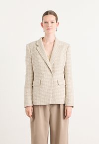 Beige tweed bleiseri, notched lapels, kaksi etutaskua, tekstuurinen kangas. Yhdistetty vaaleanbeigeihin housuihin, minimalistinen muotoilu, istuva malli.