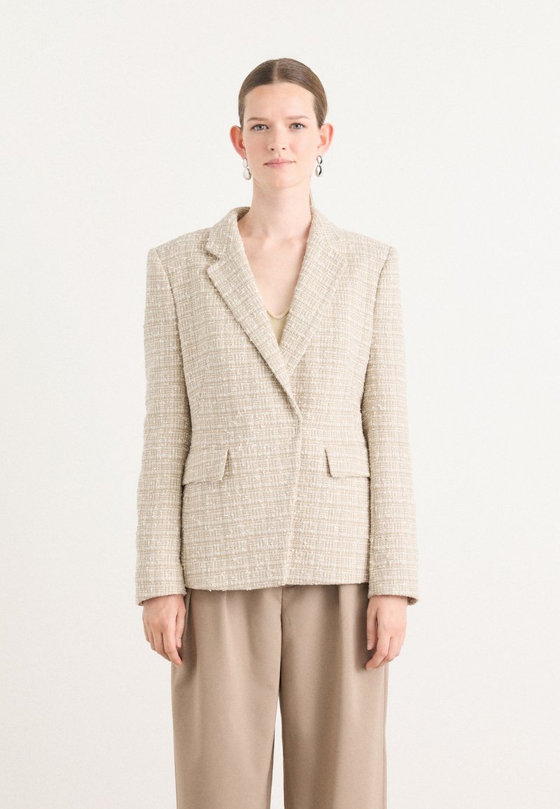 Beige tweed bleiseri, notched lapels, kaksi etutaskua, tekstuurinen kangas. Yhdistetty vaaleanbeigeihin housuihin, minimalistinen muotoilu, istuva malli.