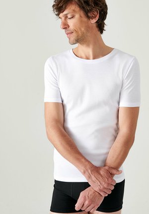 T-shirt blanc à manches courtes en coton doux, col rond, design ajusté, associé à un short noir. Texture lisse, style minimaliste.