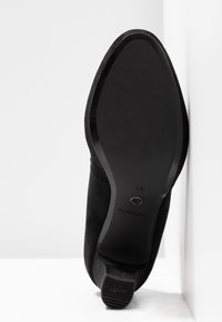 Semelle d'une bottine noire avec talon antidérapant, taille 37 indiquée, présentée sur un fond blanc en coin.