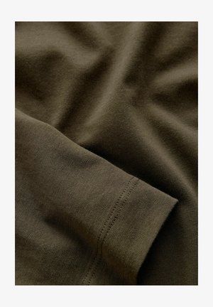 Zielono-oliwkowa bawełniana tkanina o gładkiej fakturze, z widocznym szwem wzdłuż krawędzi i delikatnymi fałdami.