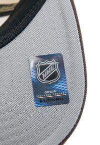 Étiquette de produit sous licence NHL présentant un logo holographique sur un fond en tissu gris avec des coutures texturées et un bord marron.