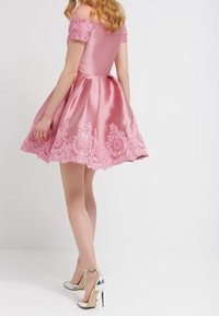 Pink satin dress with off-the-shoulder sleeves, embellished hem, and lace detailing. Paired with silver high-heeled shoes.