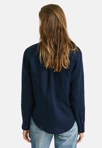 Marineblauwe linnen blouse met lange mouwen, knoopmanchetten en een afgeronde onderkant. De stof heeft een gestructureerde afwerking en een relaxte pasvorm.