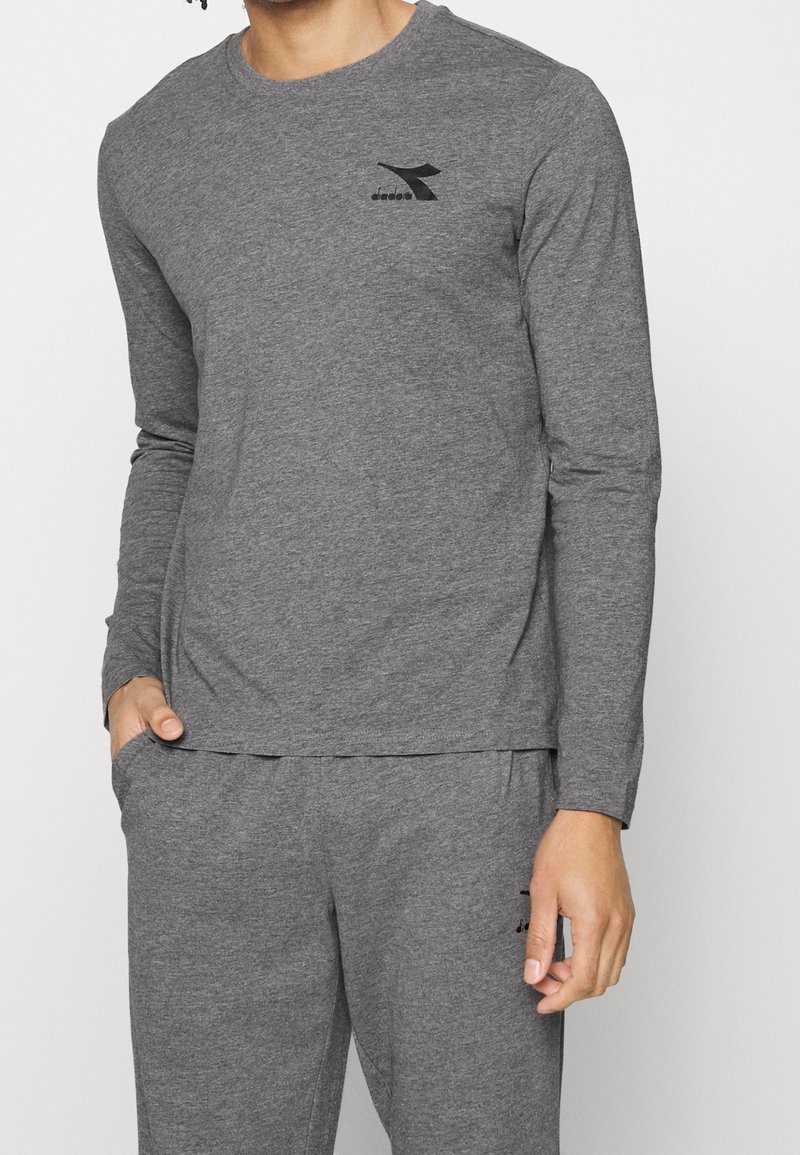 Harmaa pitkähihainen paita, joka on valmistettu pehmeästä puuvillasekoitekankaasta. Paidassa on pyöreä kaula-aukko ja pieni musta logo rinnassa.