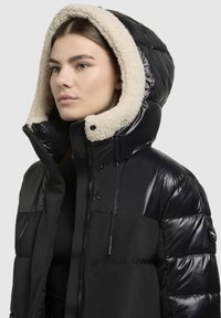 Schwarze Pufferjacke mit glänzender Oberfläche und Kapuze, die mit cremefarbenem Kunstfell gefüttert ist; verfügt über einen Reißverschluss vorne, Druckknöpfe und verstellbare Kordeln.