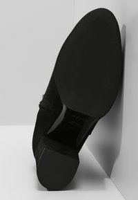 Botte de cheville en suede noir avec un bout carré, un petit talon et une semelle lisse. Dotée d'une fermeture éclair latérale pour un enfilage facile.