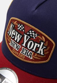 Marineblaues und rotes Cap mit gesticktem "New York"-Logo, karierten Flaggen und goldenen Akzenten. Verfügt über eine klassische strukturierte Form und Stofftextur.