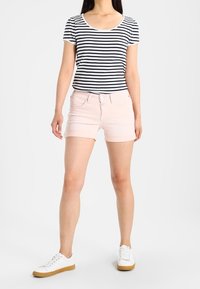 Camiseta de manga corta a rayas en azul marino y blanco combinada con pantalones cortos de mezclilla rosa claro, complementada con zapatillas blancas con suela de color tostado.