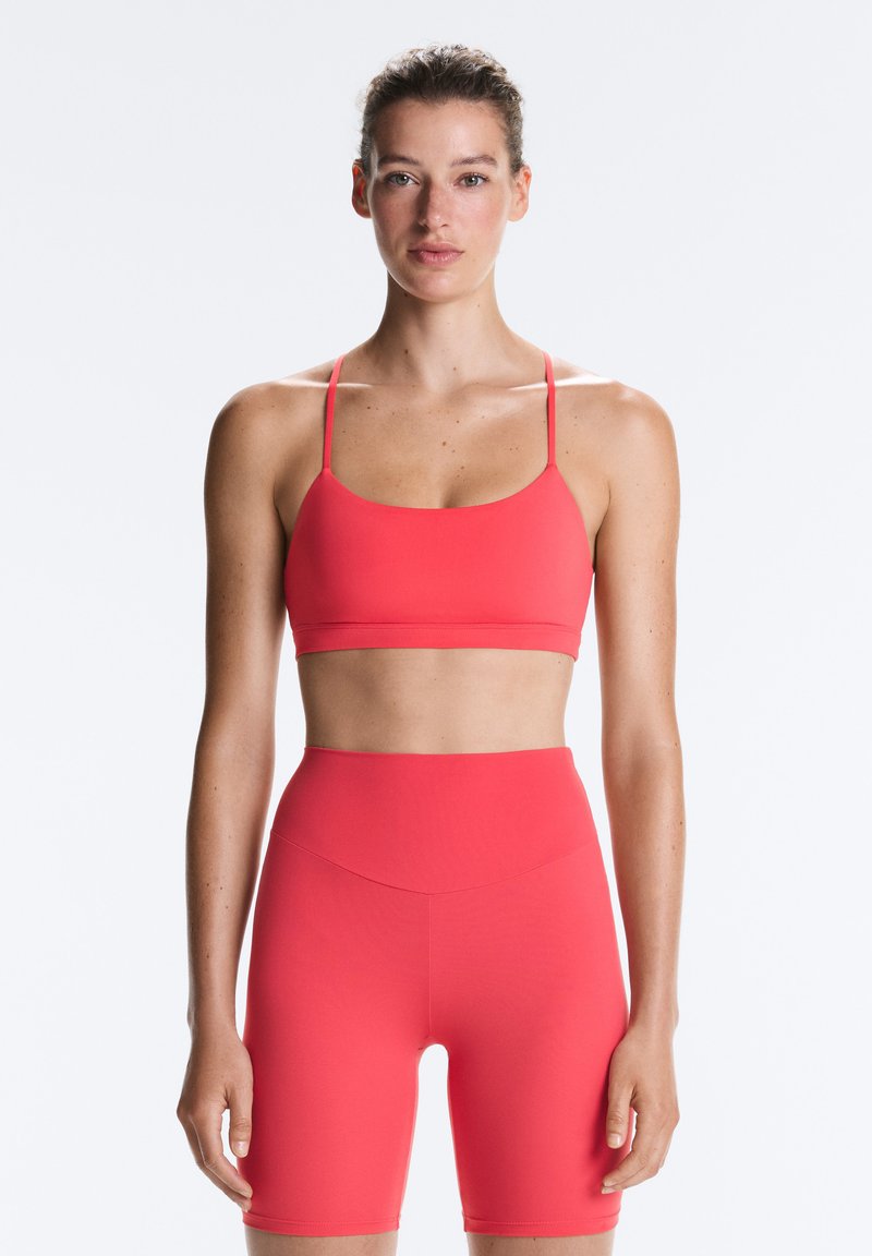 Woman facing forward, wearing a matching red sports bra and high-waisted cycling shorts against a plain light background.
