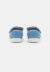 Blaue Lederschuhe mit weißen Gummisohlen, featuring einem geschlossenen Rücken, auffälligen Nähten und einem Klettverschluss-Riemen für einen sicheren Sitz.