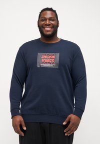 Marineblaue Sweatshirt mit langen Ärmeln, gerippten Bündchen und Saum, mit einem rechteckigen Grafikdruck in Rot und Schwarz mit "JACK & JONES."