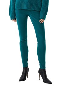 Jeans ajustados en color verde azulado, fabricados con una suave mezcla de algodón, con una textura lisa y detalles de costura, combinados con botas de tacón negro.