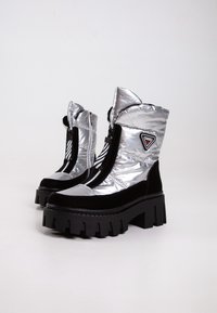 Bottes de cheville argentées, rembourrées, avec fermeture éclair, accents en cuir suédé noir, et une semelle en caoutchouc épaisse dotée d'un bord cranté. Détail du logo en triangle inclus.