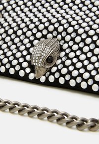 Pochette nera con decorazioni di perle e cristalli, caratterizzata da una fibbia a forma di uccello in argento dettagliata e da una tracolla a catena metallica.