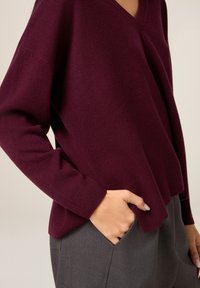Maglione bordeaux con scollo a V, maniche lunghe, tessuto morbido, vestibilità comoda, abbinato a pantaloni grigi con tasca laterale.