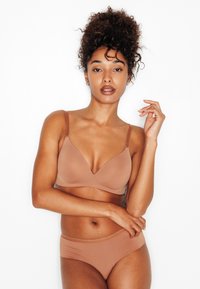 Reggiseno beige chiaro con scollo a V profondo e spalline regolabili, abbinato a slip bikini senza cuciture coordinati. Texture liscia con dettagli minimi.