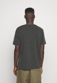 Camiseta de algodón negra con mangas cortas, cuello redondo y un corte relajado. Detalle de costura sutil en la parte posterior y una textura suave y desgastada.