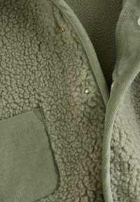Green fleece jacket featuring a soft, textured surface, corduroy pocket, and snap closures along the front.