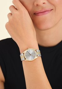 Orologio argento con quadrante rotondo, accenti dorati e bracciale in metallo bicolore. Presenta un design minimalista con display della data alle 3.