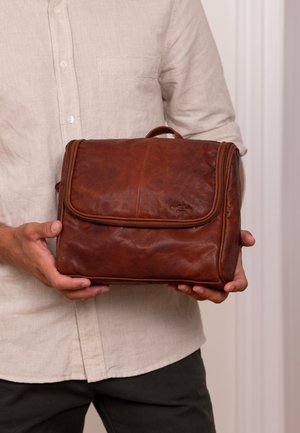 Braune Lederhandtasche mit Klappenverschluss, Reißverschlussdetails und einem oberen Griff. Glatte Textur mit matter Oberfläche und dezentem Logo-Prägung auf der Vorderseite.