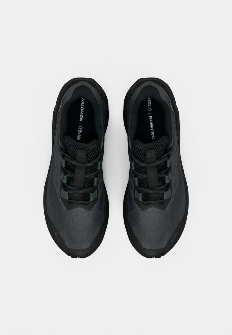 Un paio di scarpe da corsa Salomon nere con tessuto in rete e lacci, viste dall'alto su uno sfondo bianco.