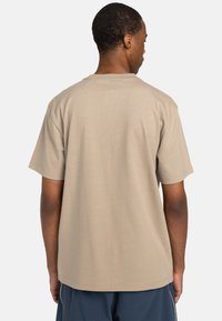 Beige Baumwoll-T-Shirt mit kurzen Ärmeln, einem standardmäßigen Rundhalsausschnitt und einem lockeren Schnitt; glatte Textur ohne bemerkenswerte Akzente oder Muster.