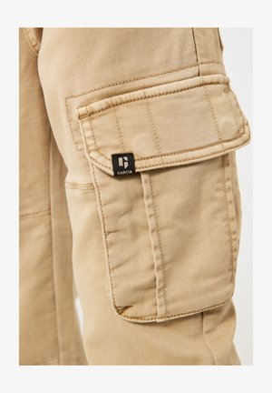 Lichtbeige cargobroek met een zijzak, nette stiknaden en een zwart label met de merknaam "GARCA." Duurzaam katoen materiaal.
