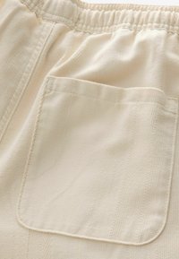 Šortsevi s elastičnim strukom od off-white tkanine, s teksturiranim uzorkom i jednim zakrpanim džepom na stražnjoj strani.
