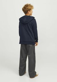 Felpa blu navy con cappuccio, maniche lunghe e vestibilità morbida, abbinata a pantaloni larghi grigio scuro e sandali. Texture del tessuto liscia.