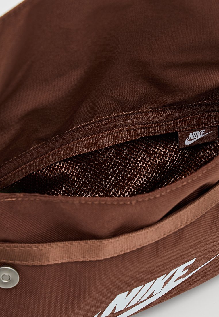 Bolsa marrón de Nike con un interior texturizado y un material exterior liso. Cuenta con un logo blanco y un cierre de cremallera con un botón a presión.