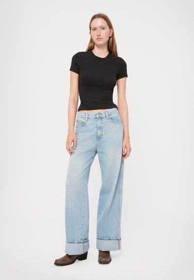 Black short-sleeved fitted top paired with wide-leg light blue denim jeans, cuffed at the ankles, worn with brown block-heeled boots.