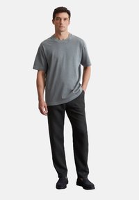 T-shirt en coton gris à manches courtes, col rond, coupe décontractée, associée à un pantalon noir et des chaussures noires, sur un fond uni.