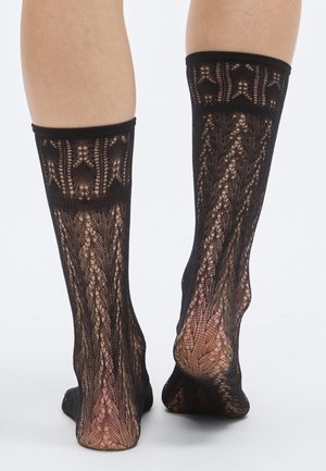 Les chaussettes hautes noires en dentelle présentent des motifs complexes, une texture transparente et un bandeau élastique confortable au sommet.