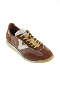 Zapatilla marrón y beige con cordones amarillos, logo blanco en el lateral, franja azul en la suela y etiqueta "victoria" en la lengüeta, inclinada hacia la izquierda.