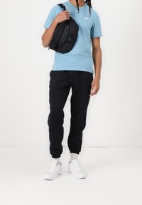 Světle modré tričko s logem Nike, černá taška přes rameno, černé tepláky a bílé tenisky s šedými akcenty. Sportovní ležérní outfit.