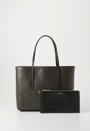 Bolsa tote negra con patrón geométrico, detalles dorados y dos asas, acompañada de una funda negra con cremallera y logo. Textura suave.