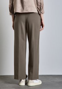 Wide-leg trousers in olive green fabric with side pockets. Paired with white low-top sneakers featuring a grey accent.