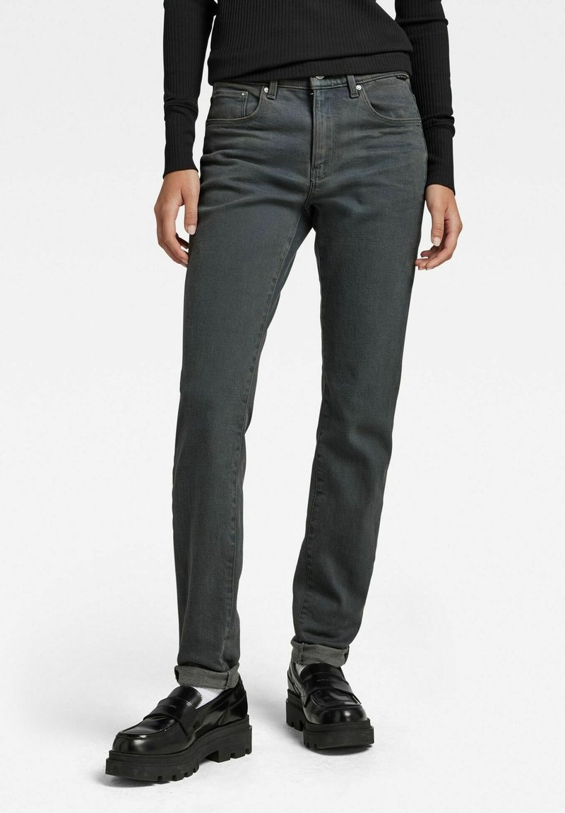 Jeans de mezclilla gris oscuro con un corte slim, diseño de cinco bolsillos y detalles metálicos. Llevados con zapatos de plataforma negros.