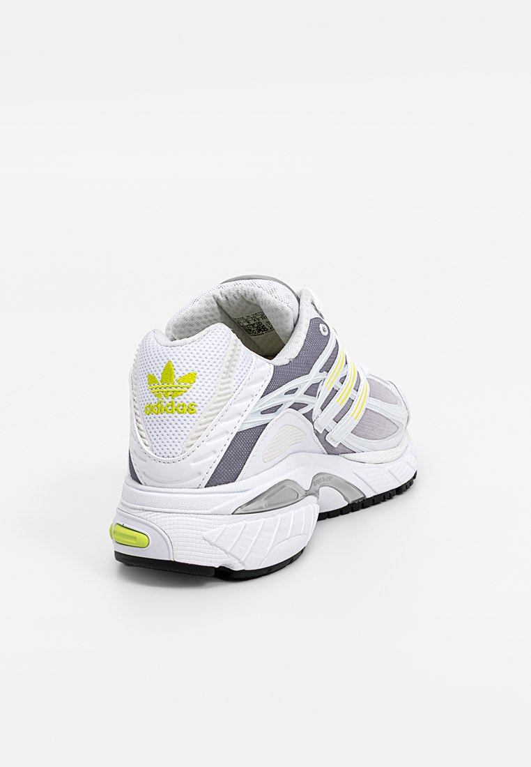 Zapatilla deportiva blanca y gris con paneles de malla, tres rayas amarillas, collar acolchado y suela de goma texturizada. Presenta un logo en el talón.