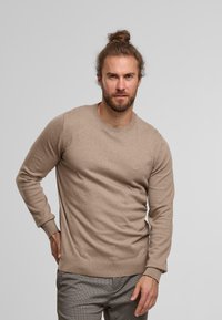 Suéter beige de cuello redondo en una suave mezcla de lana, con mangas largas y puños y dobladillo acanalados, con un sutil detalle de logo en el pecho.