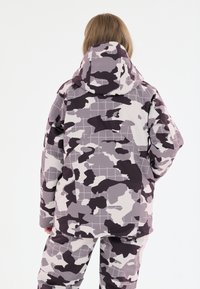Violetti ja harmaa camouflage-kuvioinen puffatakki hupun kanssa, teksturoitu kangas, ruudulliset yksityiskohdat ja rento istuvuus, kuvattu takaa.