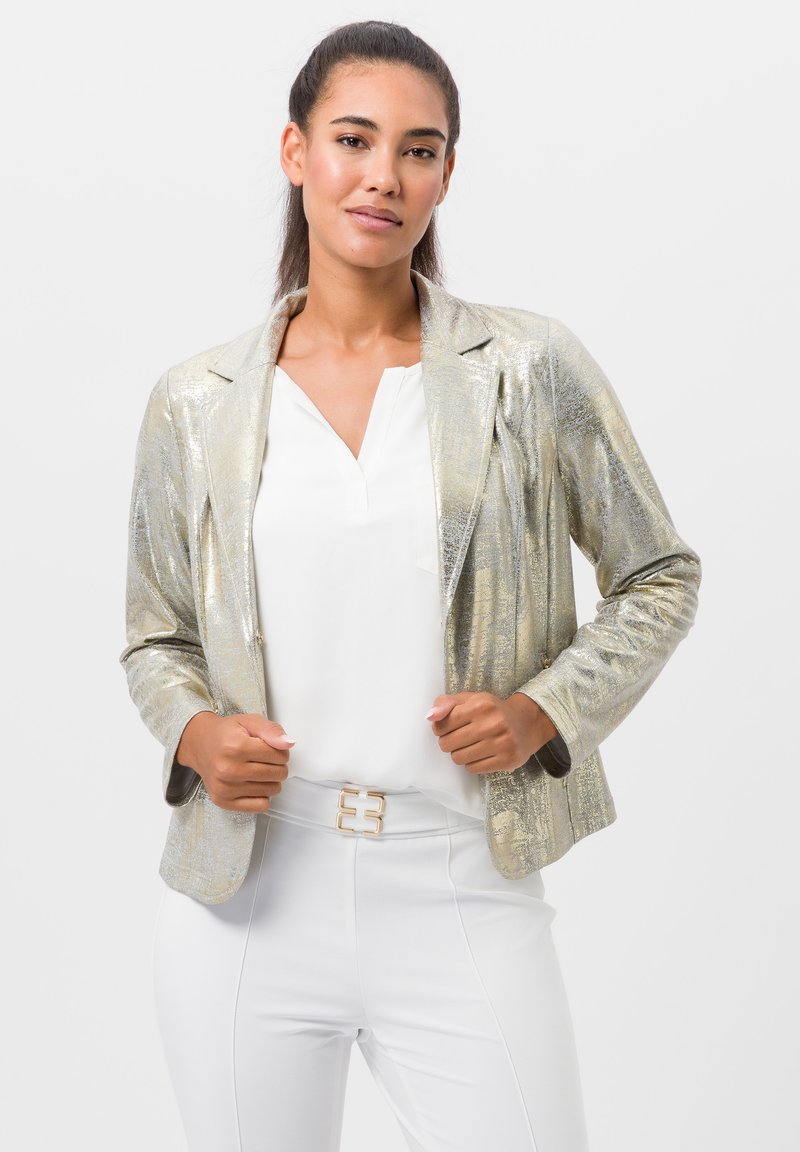 Metalen gouden blazer met een op maat gemaakte uitstraling, textuurstof, lange mouwen en ingesneden revers, gecombineerd met een witte blouse en riem.